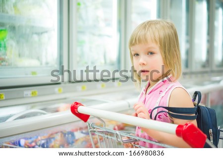 Adorable girl at shopping cart in frozen products department