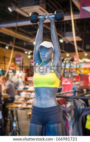 Woman mannequin in sport light suit and barbell in hand above head