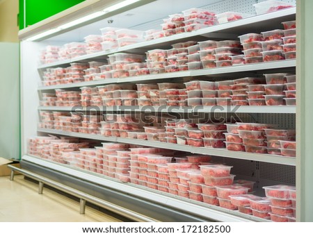 Shelves in fridge full of meat in plastic boxes in supermarket
