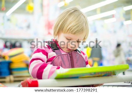 Adorable girl sit on shopping cart with kids book in supermarket