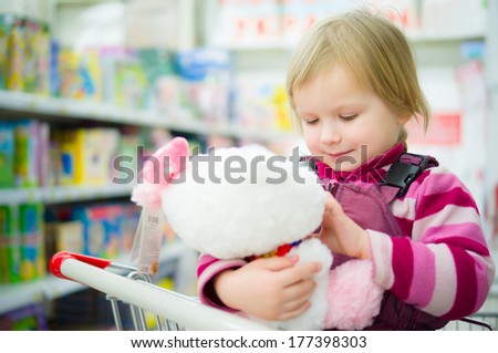Adorable girl sit on shopping cart with plush kitten toy in supermarket