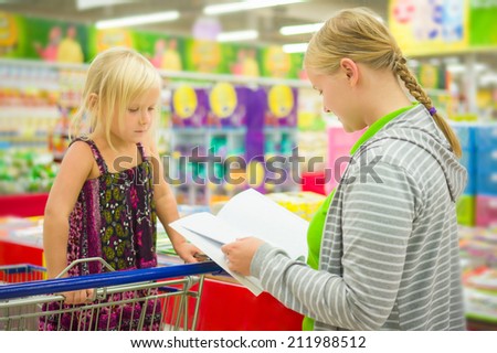 Young mother and adorable daughter in shopping cart select kids books in supermarket