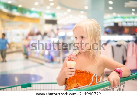Adorable girl eat fruit ice cream with rainbow sprinkles in shopping cart in supermarket