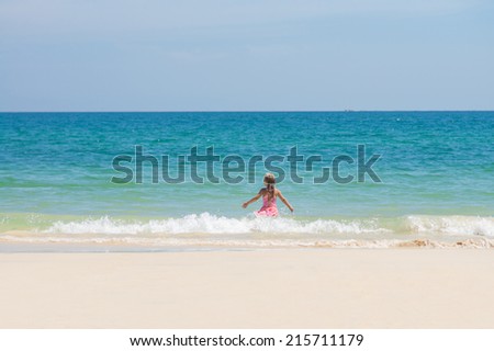 Adorable girl in pink swimming suit run to ocean through waves