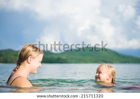 Young mother and daughter have fun swim on island in tropical ocean. Learning swim