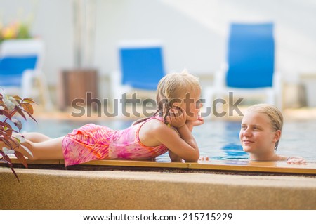 Mother in pool and daughter on pool side have fun and talk in tropical beach resort