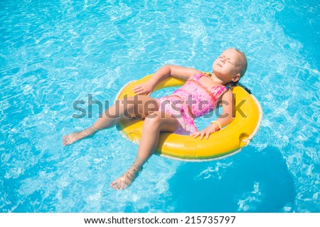 Adorable girl relax on yellow life ring in pool at tropical beach resort