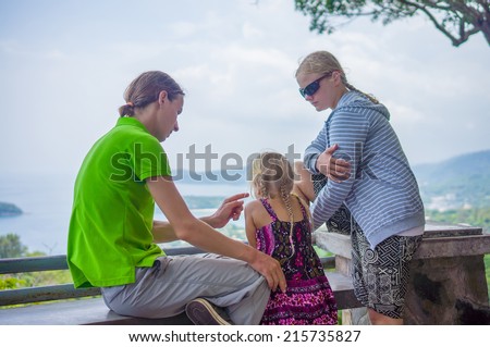 Mother, father and daughter sit on side and look around from mountain view point on tropical beach island
