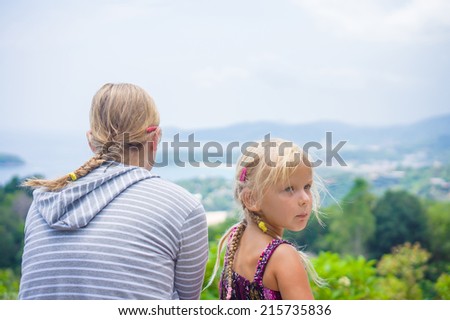 Mother and daughter look around from mountain view point on tropical beach island