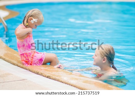 Mother and daughter with flower behind ear have fun at pool side in tropical beach resort