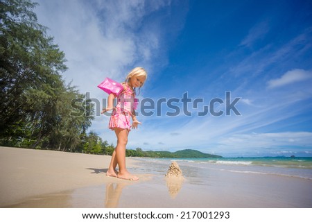 Adorable girl in pink swimming suit and inflatable arm bands build sand tower on ocean beach