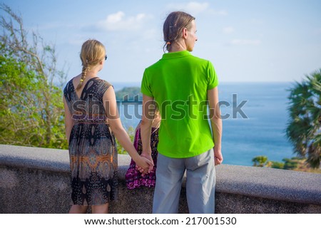 Mother, father and daughter holding hands lit with sun at side of tropical island view point