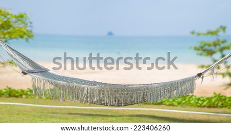 Empty hammock under palm trees at tropical beach resort with ocean on back