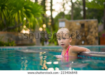 Adorable girl swim in pool at tropical beach resort . Stay at metal pool divider border