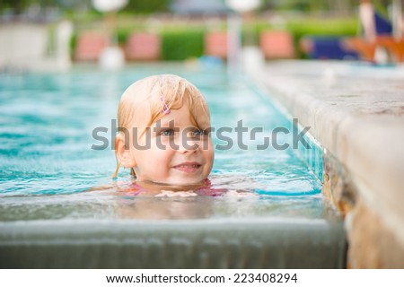 Adorable girl swim in pool at tropical beach resort. Stay in water at pool side