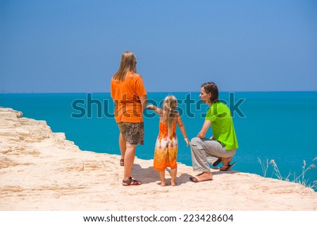 Mother, father and daughter stay on tropical island cliff and look at sea