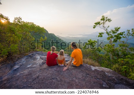 Family seat near cliff on the top of tropical island mountain on sunset