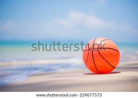 Orange ball on sand beach near ocean with waves