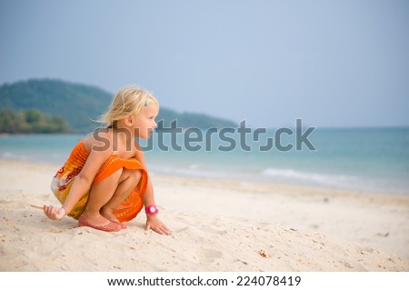 Adorable girl in orange dress play with sand on high sand ocean beach