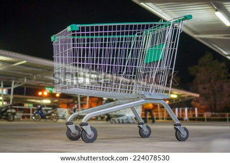 Empty shopping cart with green handle on parking near supermarket in evening