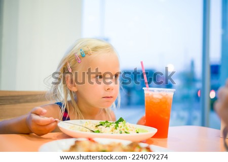 Adorable girl dinning on food court with vegetables rice and juicy drink with straw