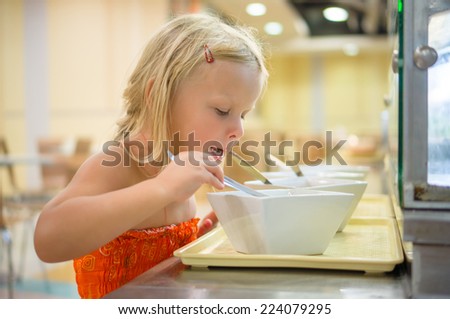 Adorable girl sniffing dishes from spoon on food court in mall