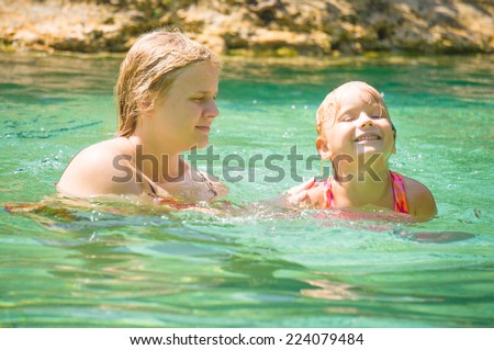 Young mother learn  daughter to swim in crystal clear laguna on tropical island