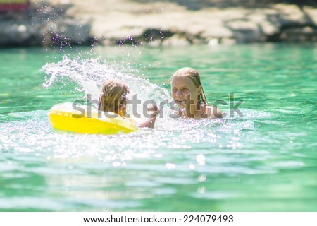 Young mother and daughter swimming with inflatable ring in crystal clear laguna on tropical island