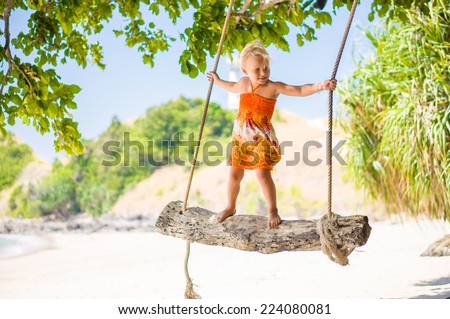 Adorable girl stay on rope swing under palm trees on tropical island