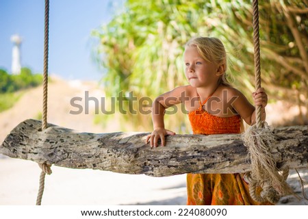 Adorable girl near rope swing under palm trees on tropical island