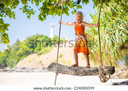 Adorable girl stay on rope swing under palm trees on tropical island