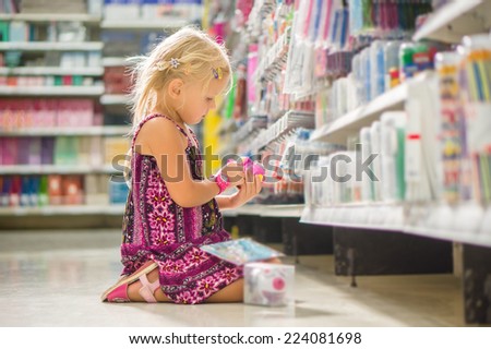 Adorable girl select pencil sharpener in stationery department sitting on floor in supermarket