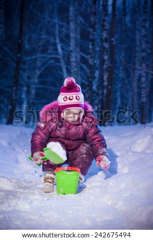 Adorable girl ride on ski and play with snow in evening park