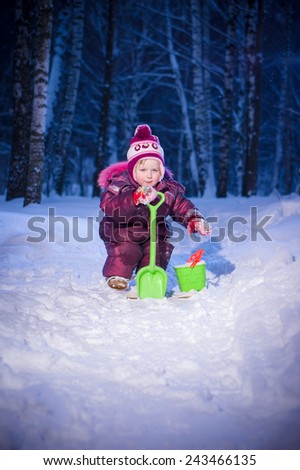 Adorable girl ride on ski and play with snow in evening park