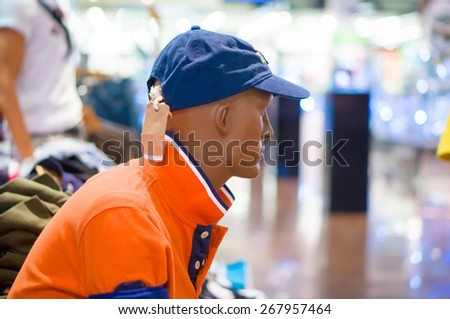 Man mannequin in orange t-shirt and cap in cloth supermarket
