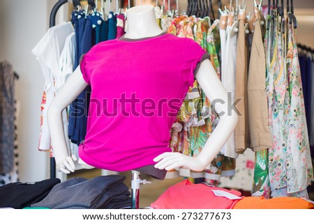 Woman mannequin in bright pink t-shirt with blouses and skirts on hangers on back