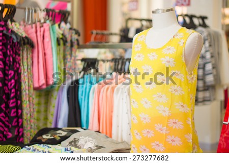 Woman mannequin in bright yellow flower pattern top and skirts with blouses on back