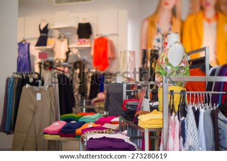 Woman mannequin in blouse and shorts with bunch of different dresses, blouses and trousers on tables and hangers around