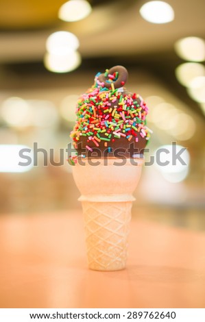 Ice cream cone with chocolate and rainbow color sprinkles on blurry background
