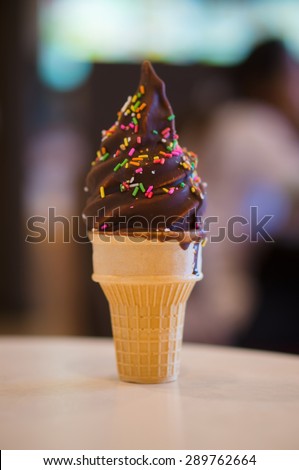Ice cream cone with chocolate and rainbow color sprinkles on blurry background