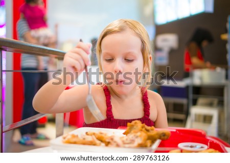 Adorable girl have meal with chicken,  soda drink and fried potatoes at fast food restaurant