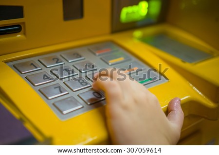 Close up of ATM keypad and hand on keys with withdrawal and card holes light on