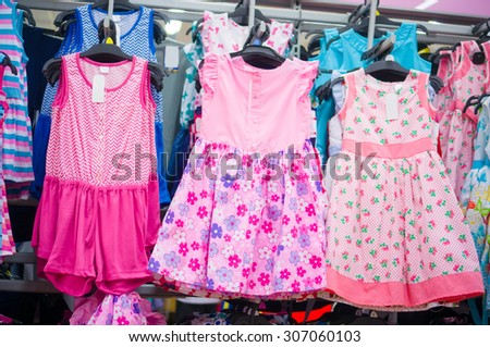 Variety of beautiful baby girl dresses on stands and hangers in supermarket
