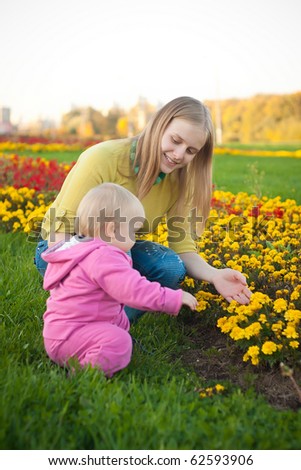 Young adorable woman show yellow flowers on bed to cute baby on sunset
