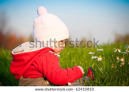 Young adorable baby sit on top of hill and touch with flowers