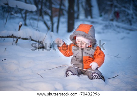 Adorable baby walking in evening park. Play with snow and branch