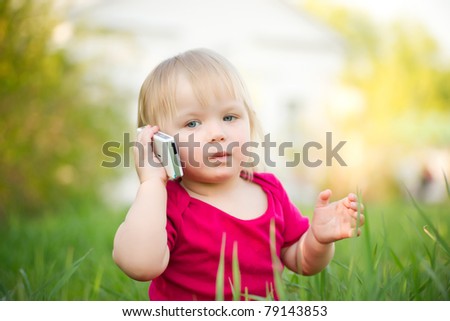 Adorable baby play with cell phone calling sitting in deep grass in park