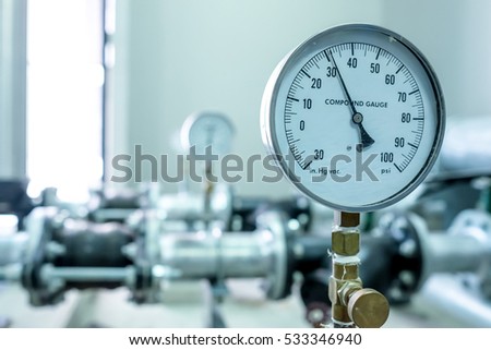 pressure compound gauge psi meter in pipe and valves of water system industrial focus left closeup white light defocus blur background