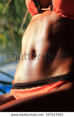 Sexy and fit belly on young woman against the sun