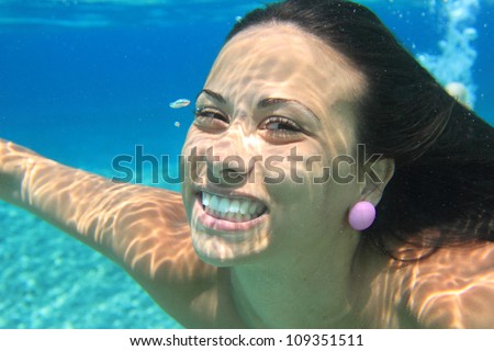 Woman swimming underwater in the sea smiling. Young female swimmer at holiday resort.